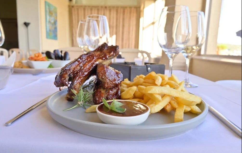 Plated grilled meat ribs with golden french fries and dipping sauce on a white plate, served on a formal dining table