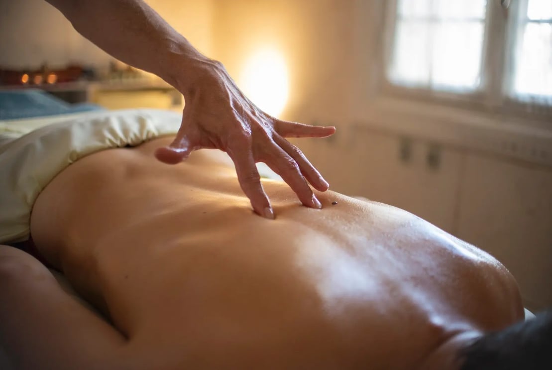 Massage therapists hands performing a back massage on a client in a wellness spa setting with warm lighting